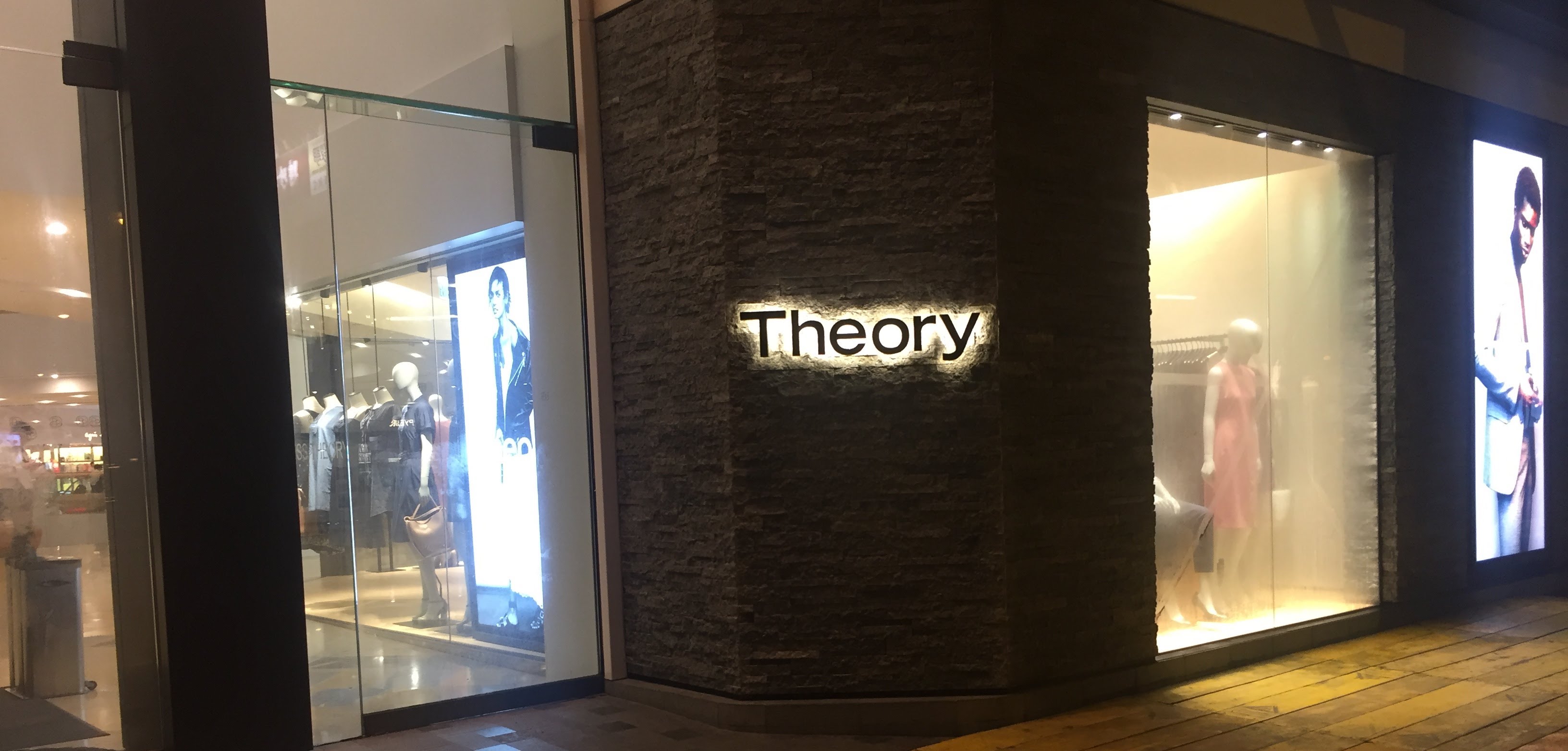 Picture of a retail clothing
      storefront with the word Theory on the wall. Picture is nighttime in Hong Kong
      with the store interior glowing through the windows and the Theory sign is backlit
      against the wall.
